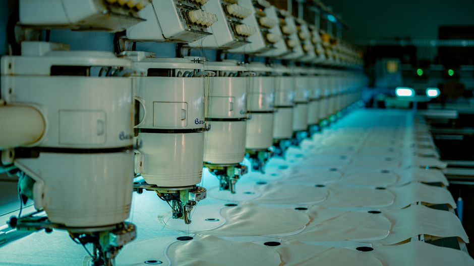 Row of industrial sewing machines in a textile factory producing garments.